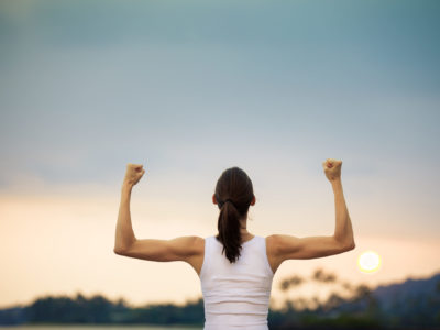 photo of a strong woman with arms uplifted celebrating sustainable weight loss in front of a sunset