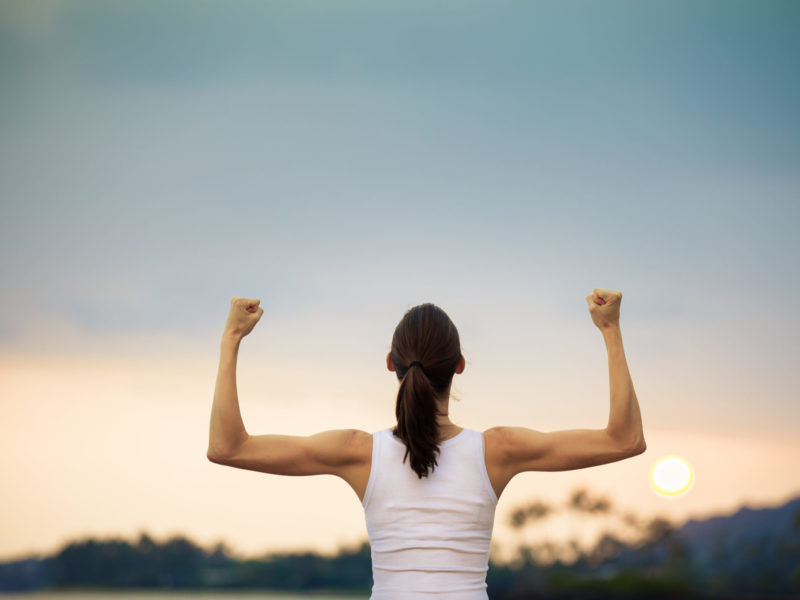 photo of a strong woman with arms uplifted celebrating sustainable weight loss in front of a sunset